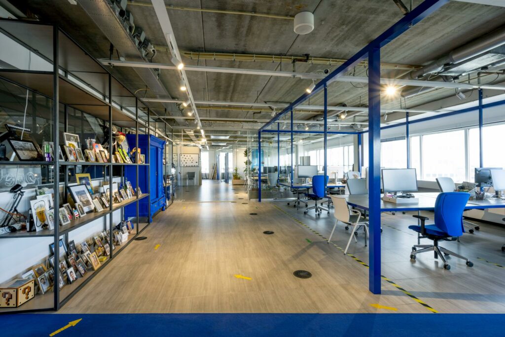 Modern en licht kantoorinterieur aan de Johan Huizingalaan met open werkplekken, blauwe accenten en persoonlijke fotolijstjes op open planken.